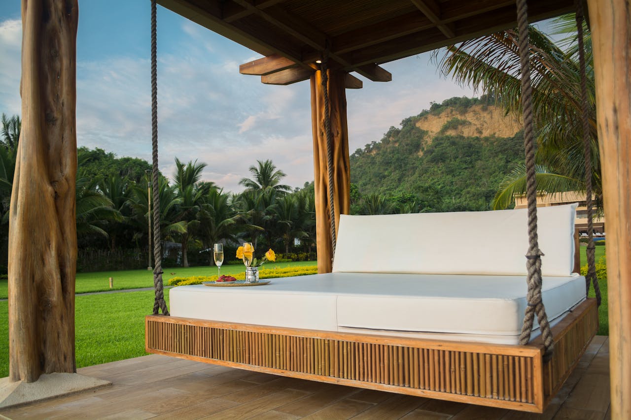 Services A luxurious swing bed under a wooden canopy with tropical palm trees.